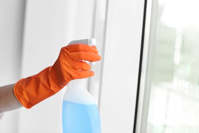 Photo of Cleaner washing window glass with detergent indoors, closeup