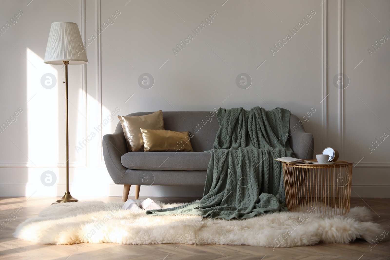 Photo of Stylish room interior with comfortable sofa, knitted blanket and coffee table near white wall