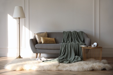 Photo of Stylish room interior with comfortable sofa, knitted blanket and coffee table near white wall