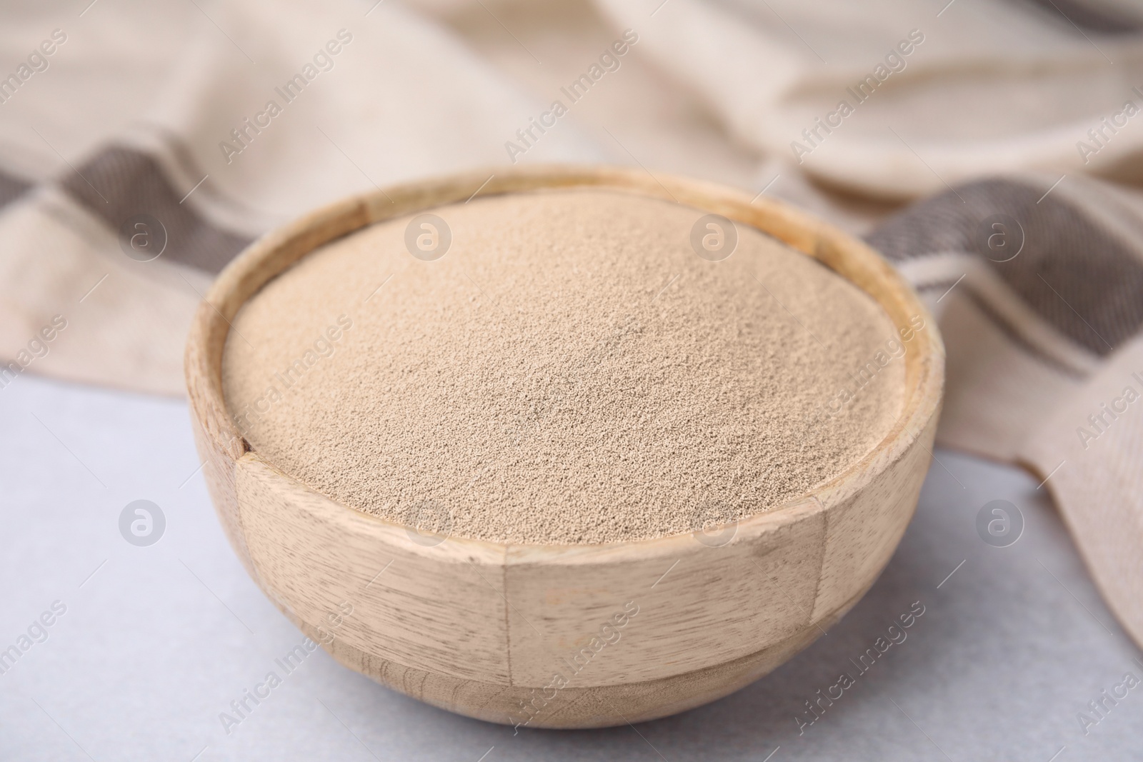 Photo of Granulated yeast in wooden bowl on light gray table, closeup