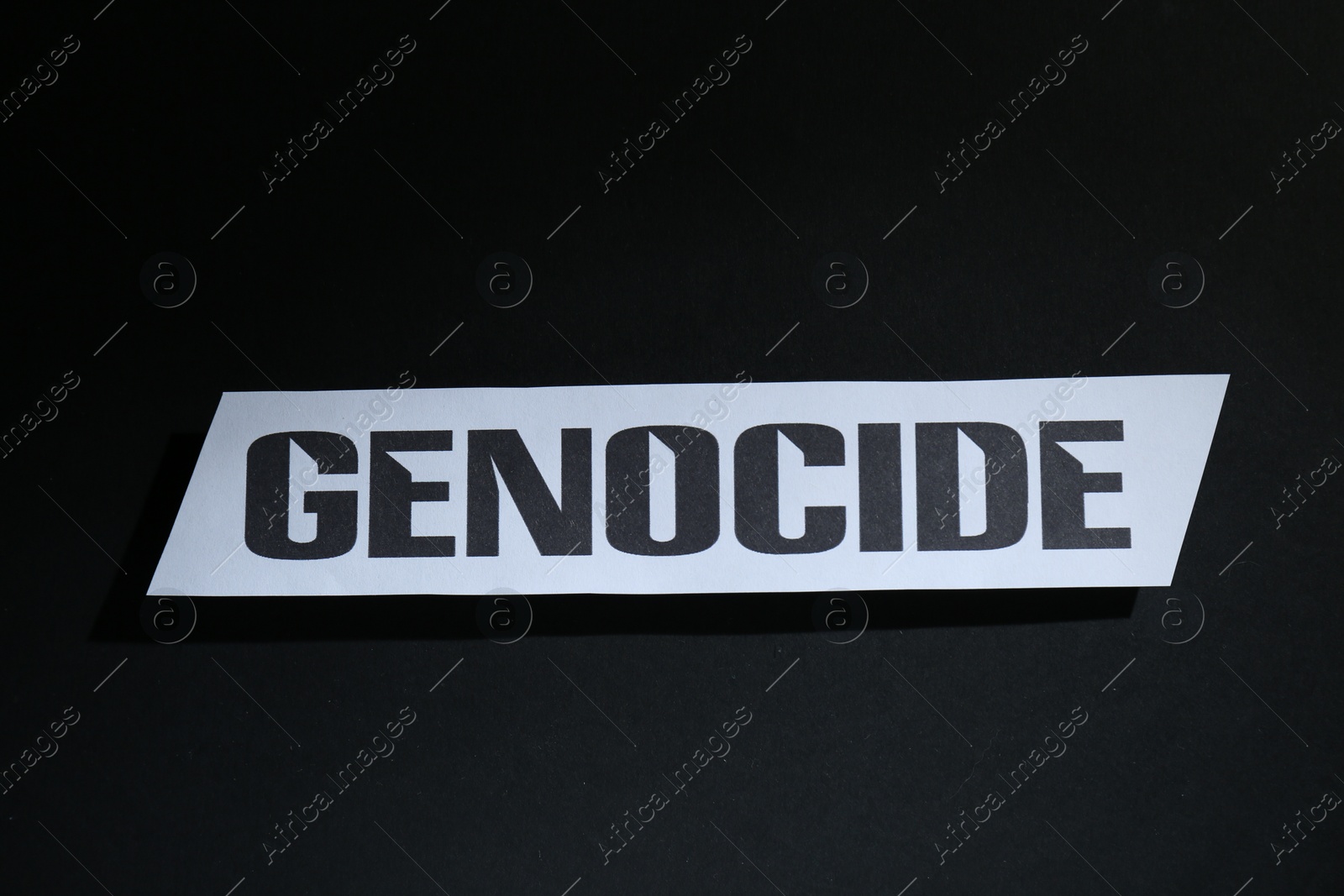 Photo of Paper with word Genocide on black background, top view