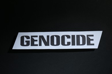 Photo of Paper with word Genocide on black background, top view