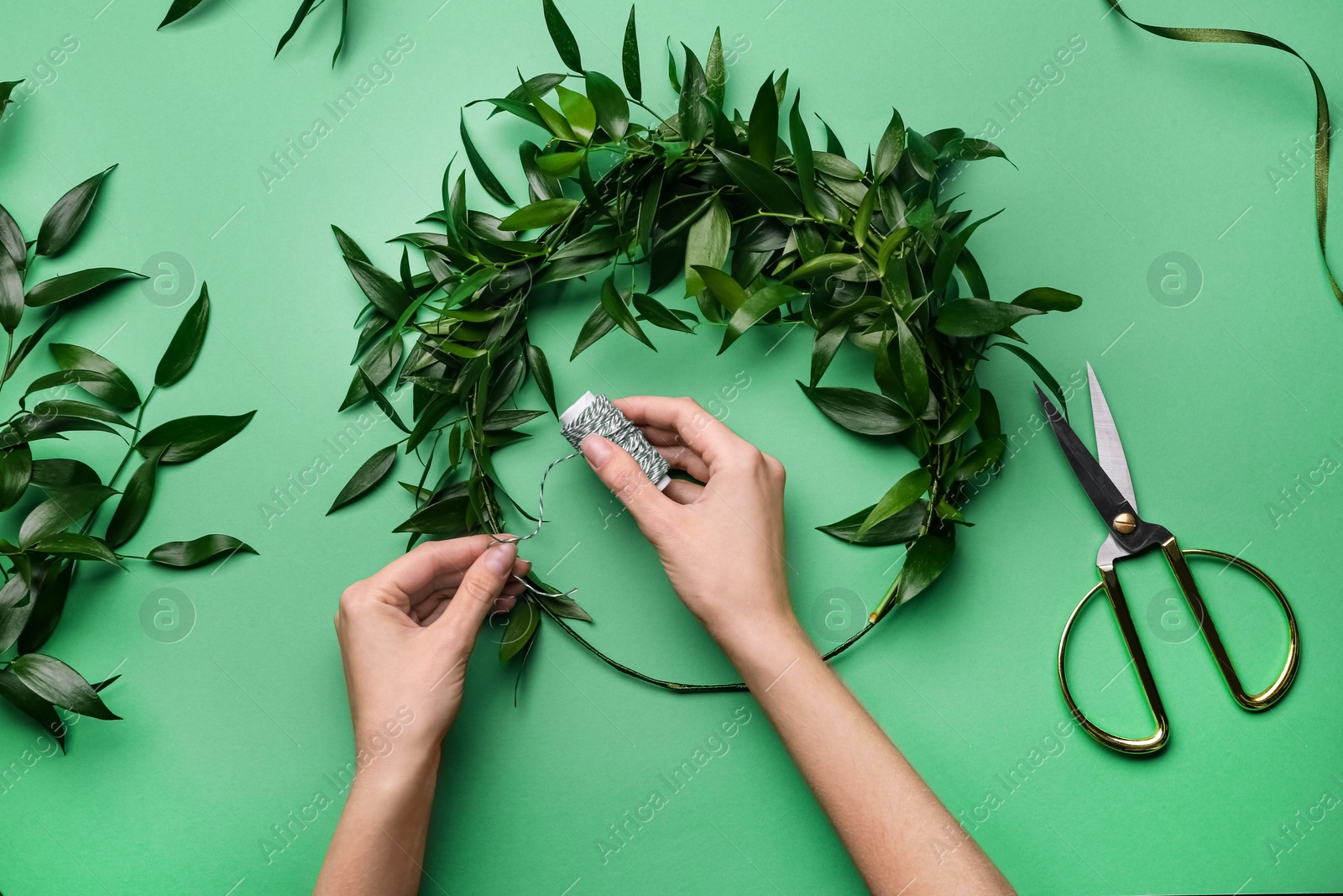 Photo of Florist making beautiful mistletoe wreath on green background, top view. Traditional Christmas decor