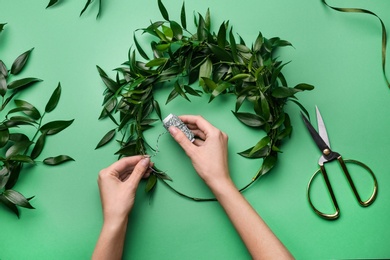 Photo of Florist making beautiful mistletoe wreath on green background, top view. Traditional Christmas decor