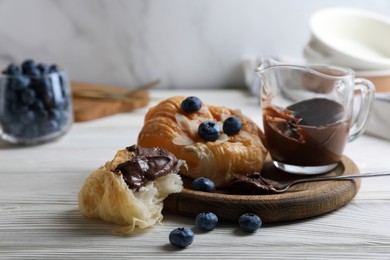 Photo of Delicious croissant with chocolate and blueberries on white wooden table, closeup