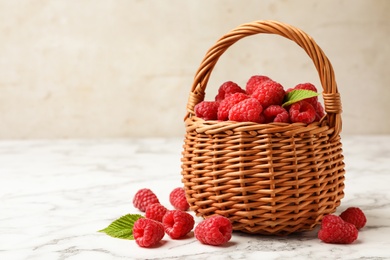 Photo of Wicker basket with delicious ripe raspberries on white marble table against light background, space for text