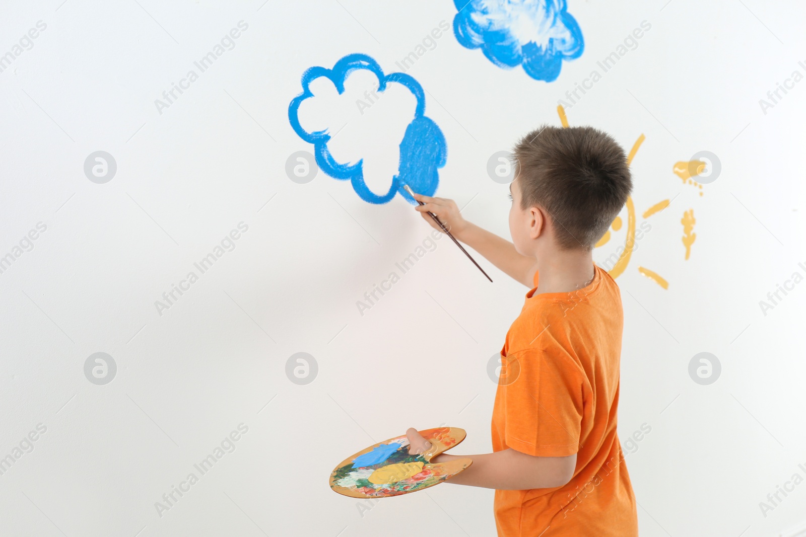 Photo of Little child painting cloud on white wall in room