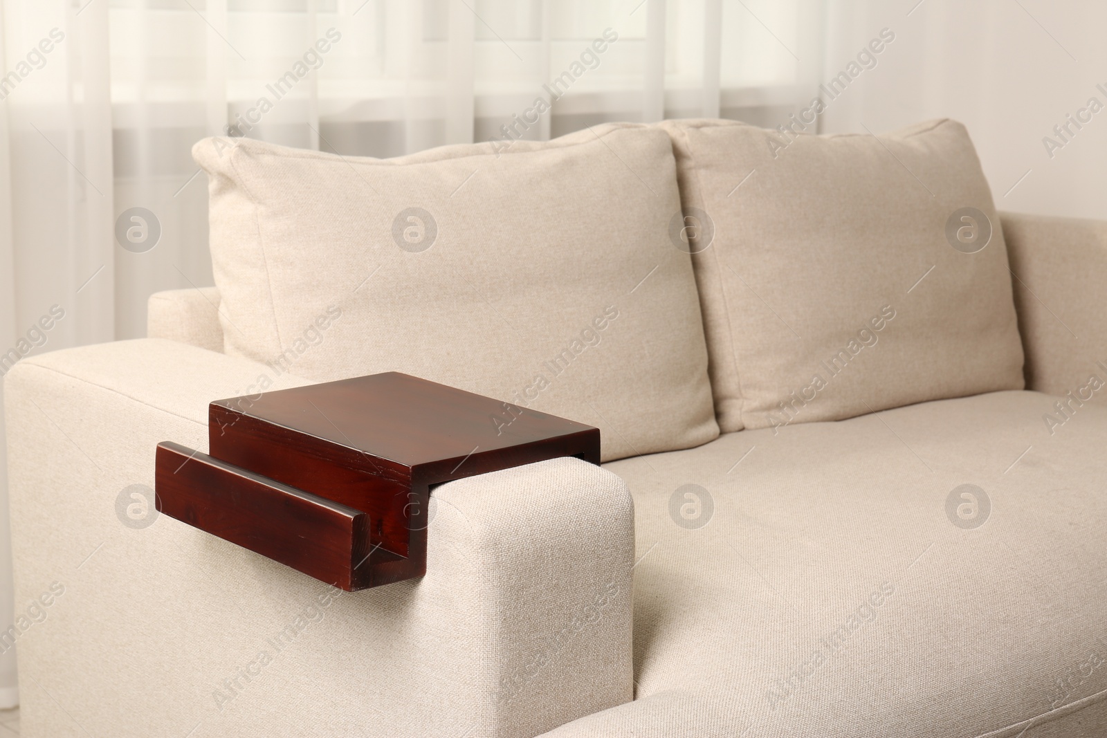 Photo of Wooden armrest table on sofa in room. Interior element