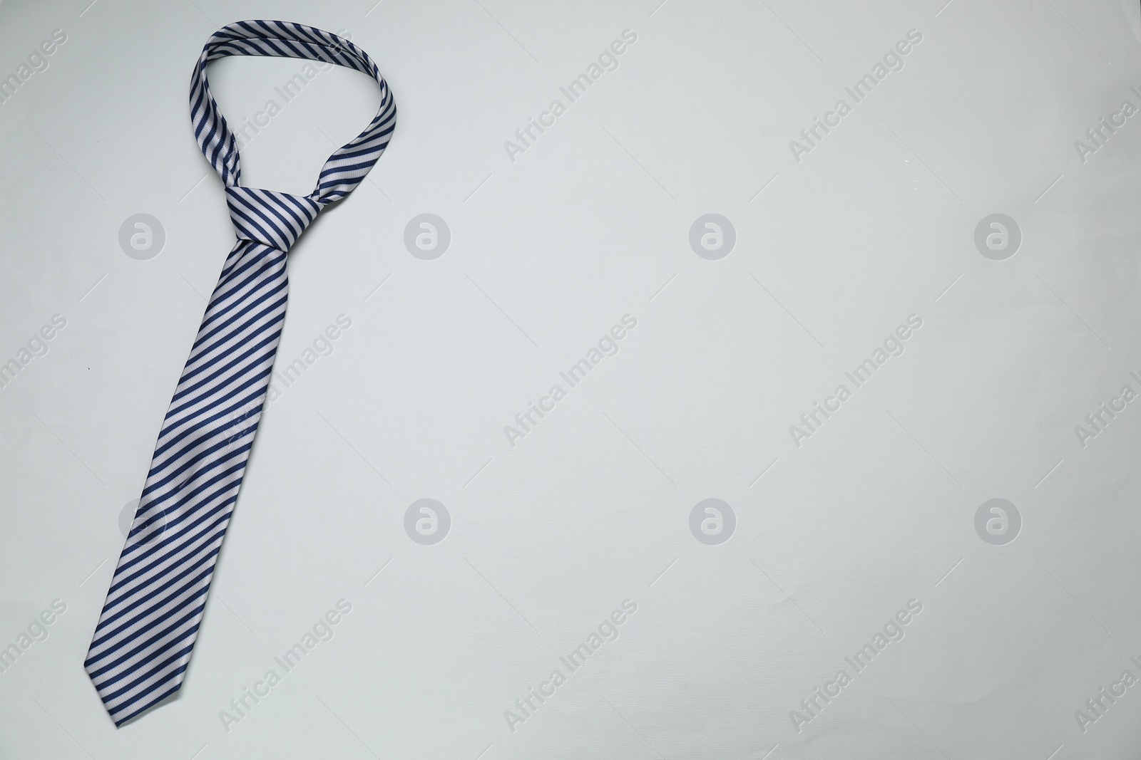 Photo of Striped necktie on light background, top view. Space for text