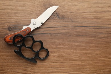 Photo of Black brass knuckles and knife on wooden background, flat lay. Space for text