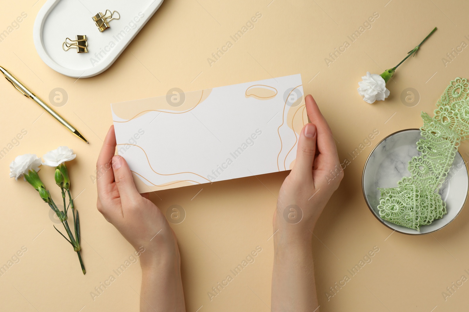 Photo of Woman holding blank invitation card on beige background, top view. Space for text