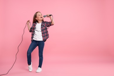 Cute little girl with microphone singing on pink background, space for text