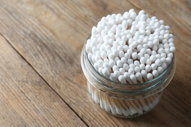Many cotton buds in glass jar on wooden table, space for text