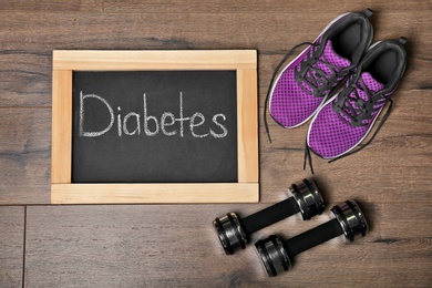 Photo of Flat lay composition with word DIABETES, sneakers and dumbbells on wooden background