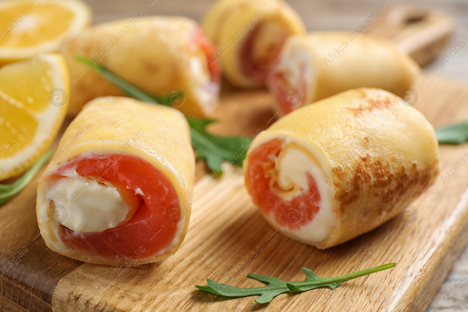 Photo of Delicious thin pancakes with salmon and cream cheese on wooden board, closeup