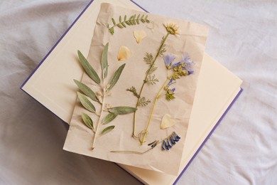 Sheet of paper with dried flowers and leaves on white fabric, top view