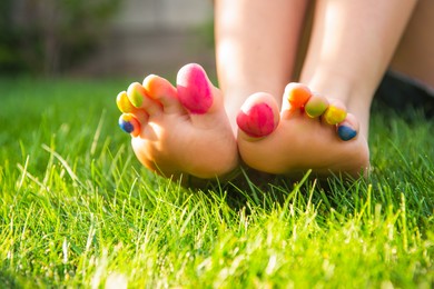 Photo of Teenage girl with painted toes sitting on green grass outdoors, closeup