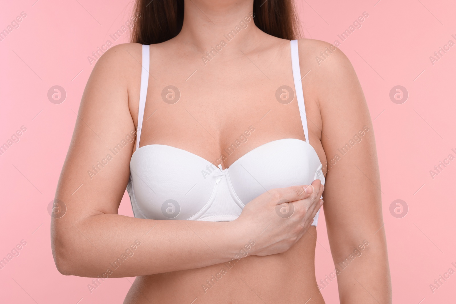 Photo of Mammology. Woman in bra doing breast self-examination on pink background, closeup