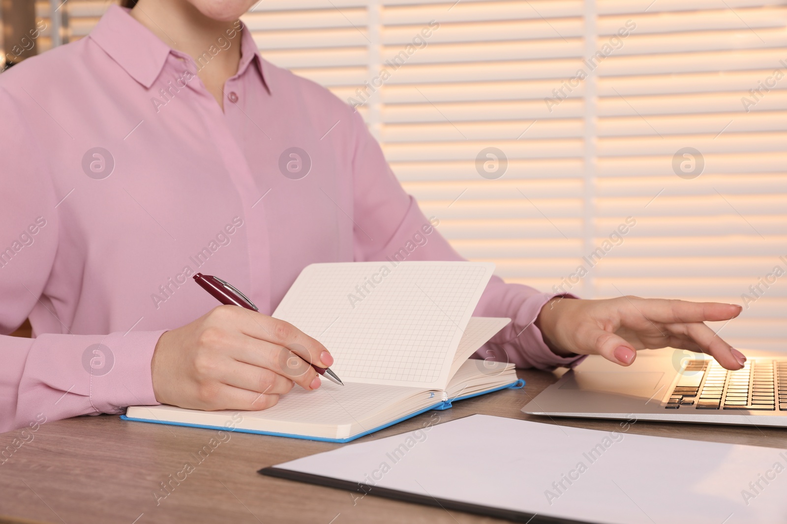 Photo of Woman taking notes at wooden table indoors, closeup