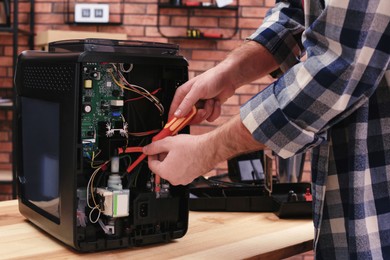 Photo of Man with screwdriver fixing coffee machine at table indoors, closeup