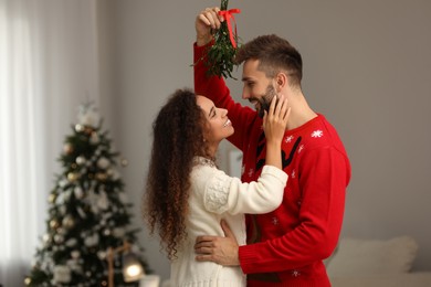 Lovely couple under mistletoe bunch in room decorated for Christmas