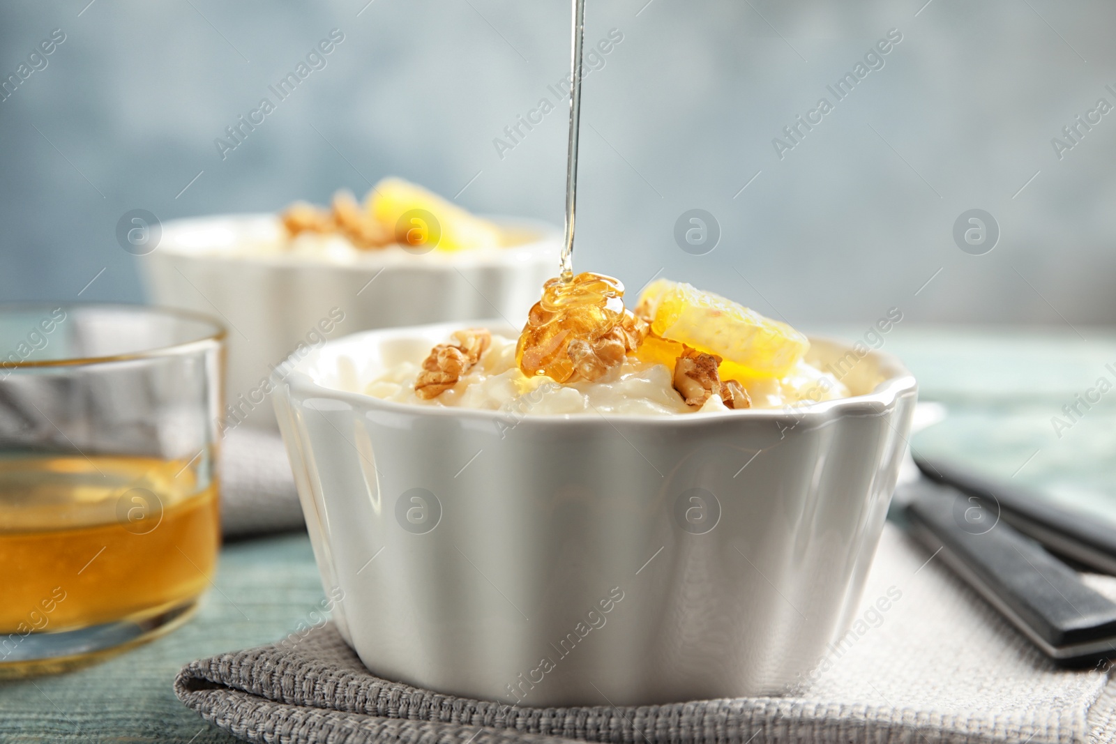 Photo of Pouring honey onto rice pudding with walnuts and orange slice in ramekin on table