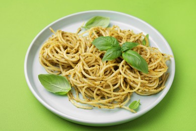 Photo of Delicious pasta with pesto sauce and basil on light green background, closeup
