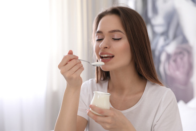 Photo of Young attractive woman eating tasty yogurt at home