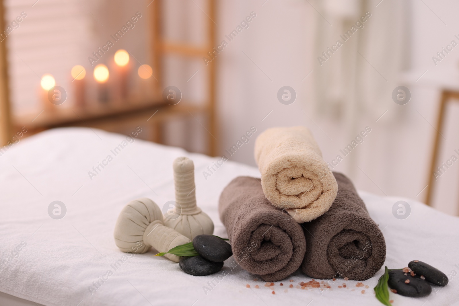 Photo of Spa stones, rolled towels and herbal bags on massage table indoors