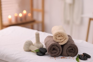 Photo of Spa stones, rolled towels and herbal bags on massage table indoors