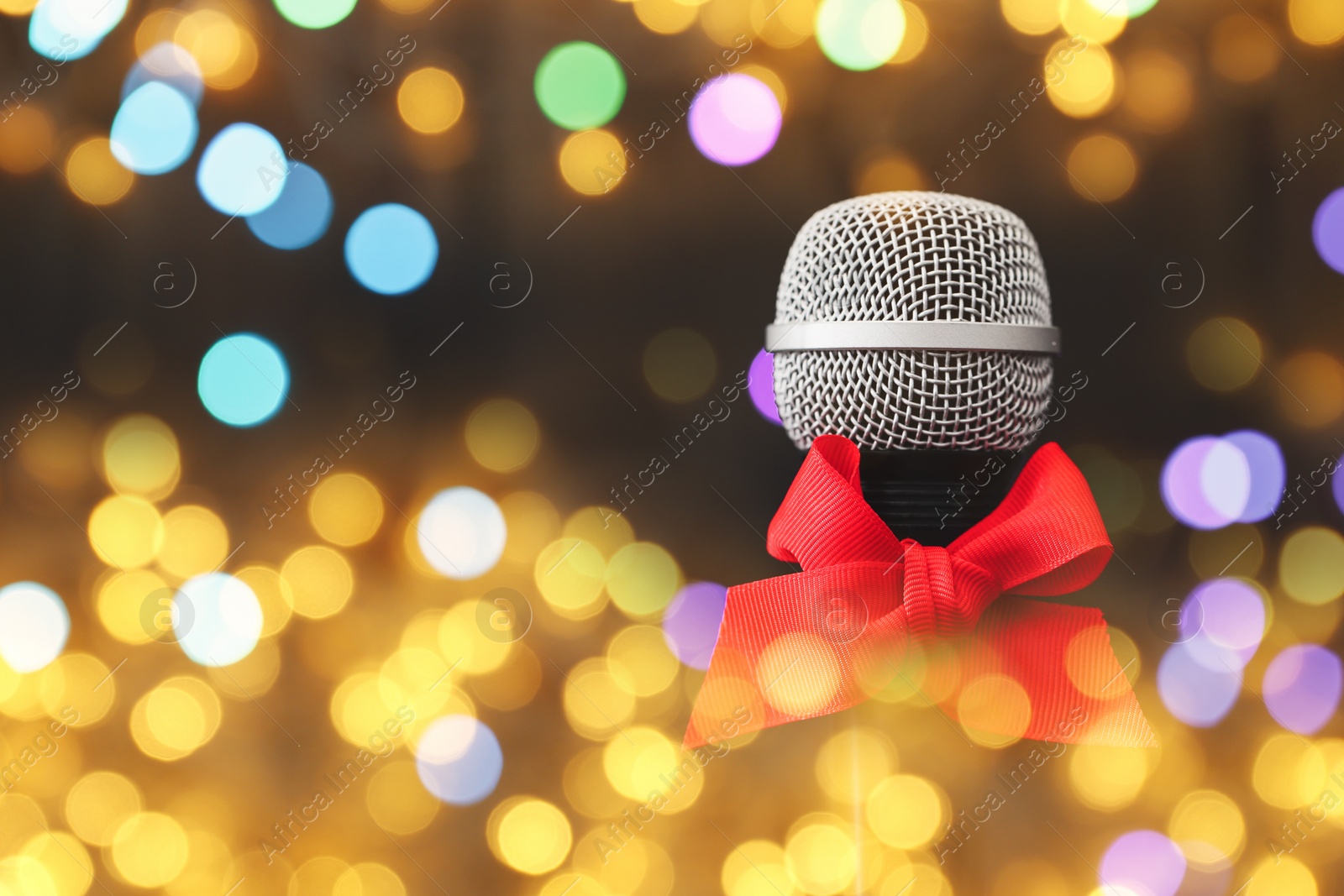 Image of Christmas and New Year music. Microphone with red bow on black background, bokeh effect