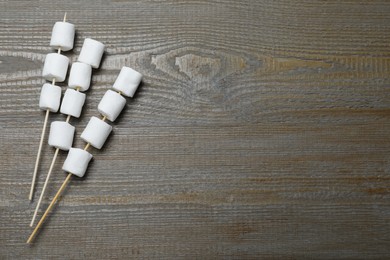 Photo of Sticks with marshmallows on wooden table, flat lay. Space for text
