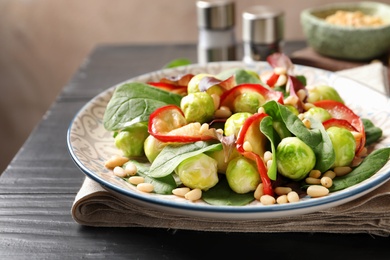 Photo of Plate of delicious salad with Brussels sprouts and roasted apples on wooden table