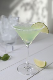 Photo of Delicious Margarita cocktail in glass and lime on white wooden table