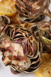Photo of Tasty grilled artichokes and lemon slices on plate, closeup