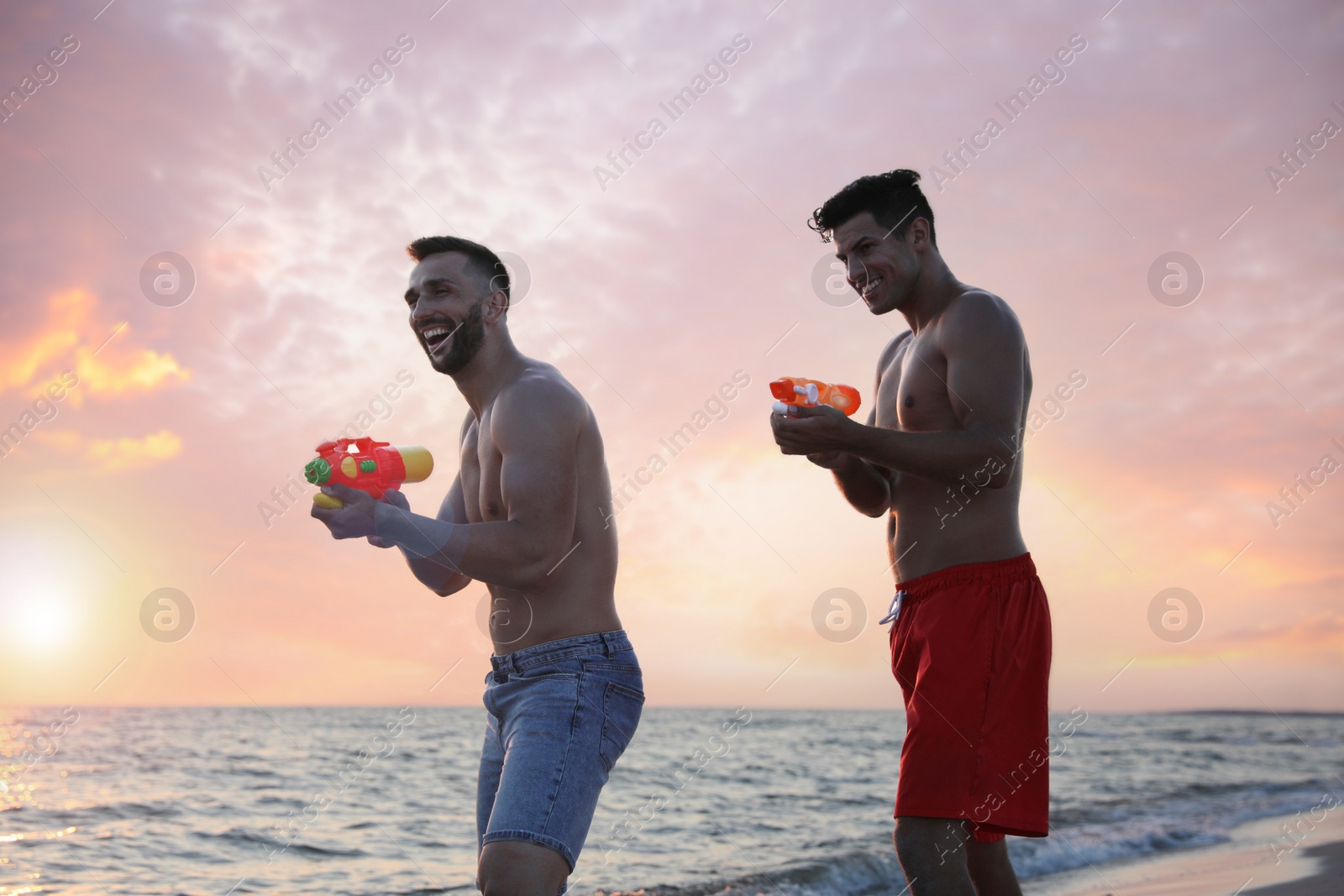 Photo of Friends with water guns having fun on beach at sunset