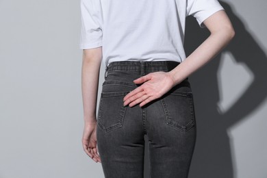 Photo of Woman showing open palm behind her back on grey background, back view