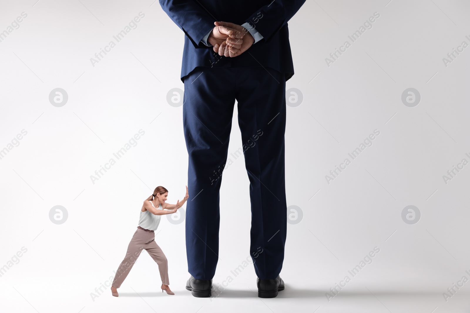 Image of Small woman pushing giant man on light background