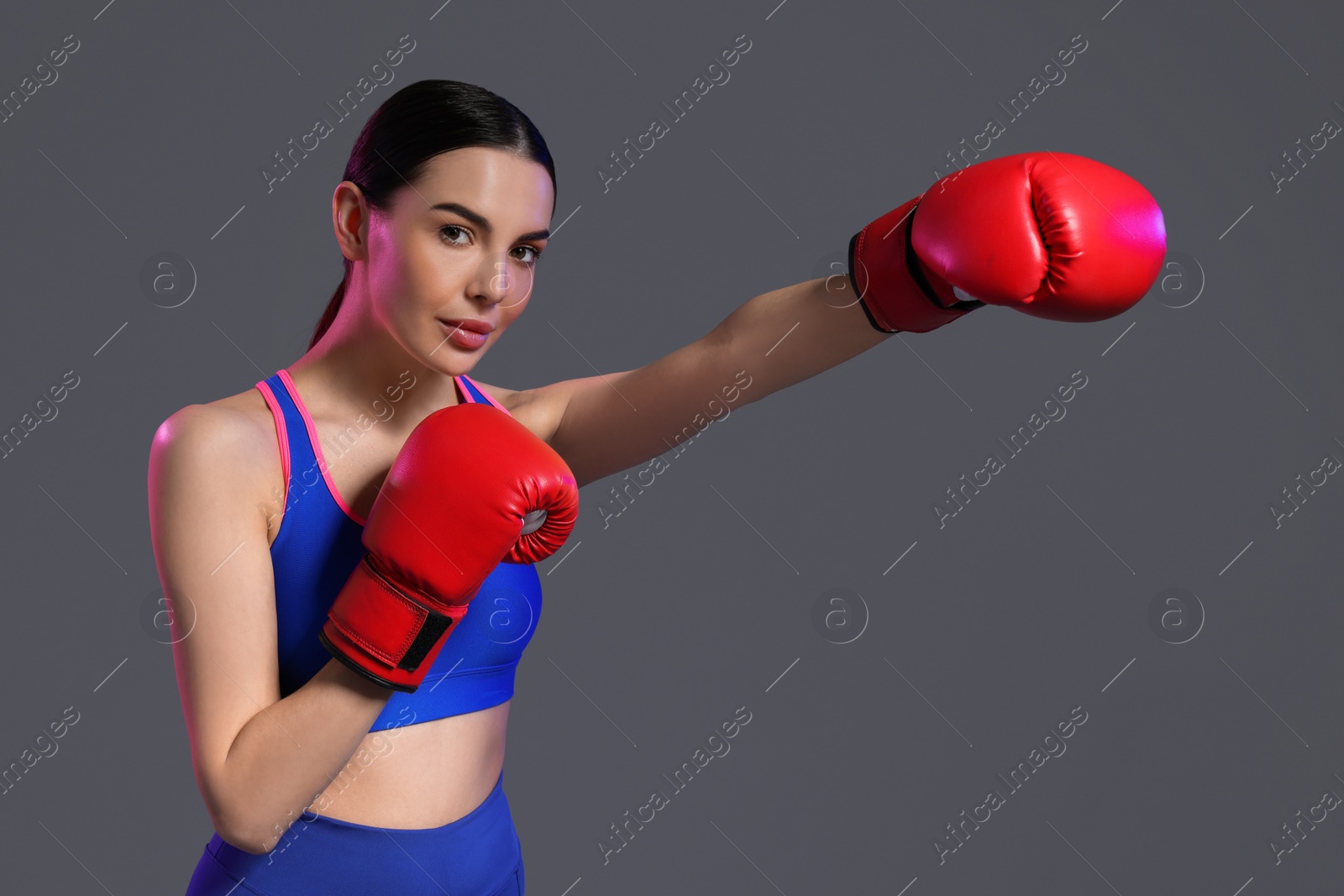 Photo of Beautiful woman wearing boxing gloves training in color lights on grey background