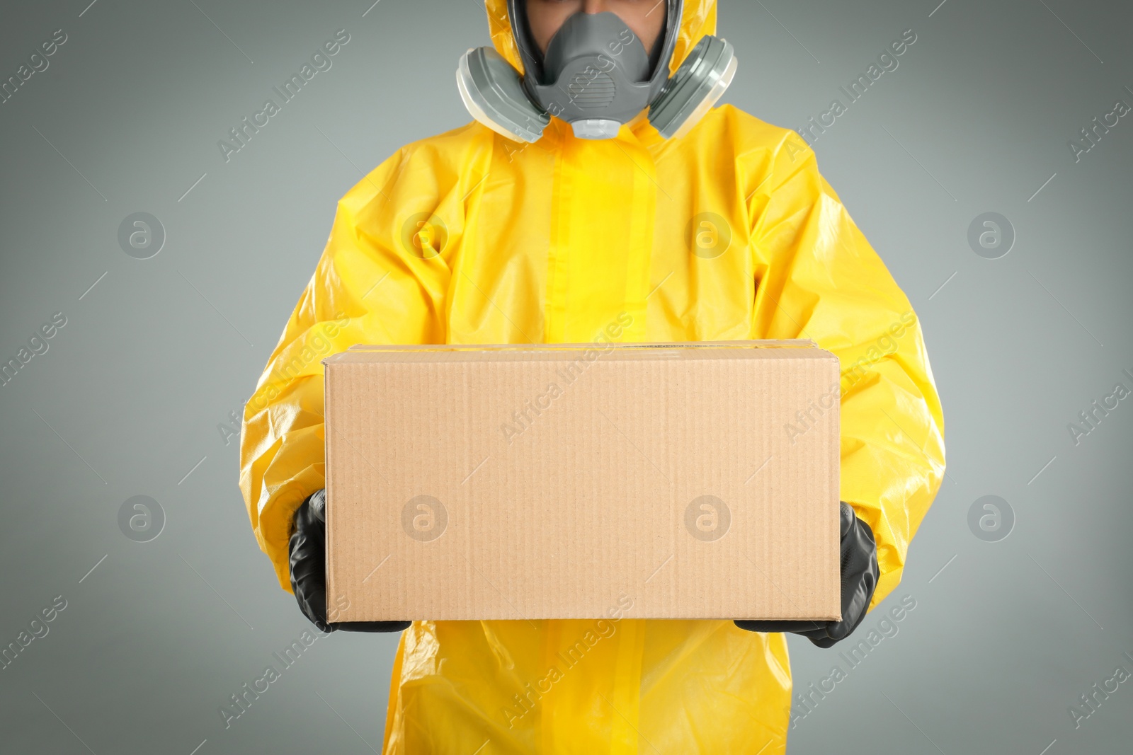 Photo of Man wearing chemical protective suit with cardboard box on light grey background, closeup. Prevention of virus spread