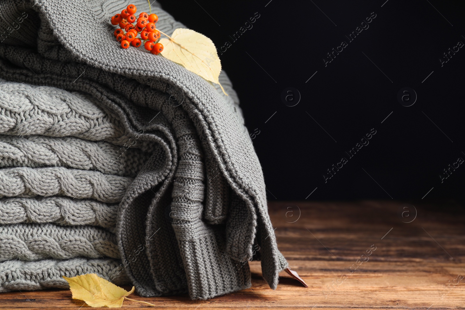 Photo of Knitted plaids with red berries and dry leaves on wooden table, closeup. Space for text