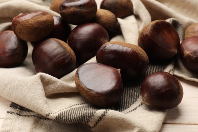 Photo of Sweet fresh edible chestnuts on light wooden table, closeup
