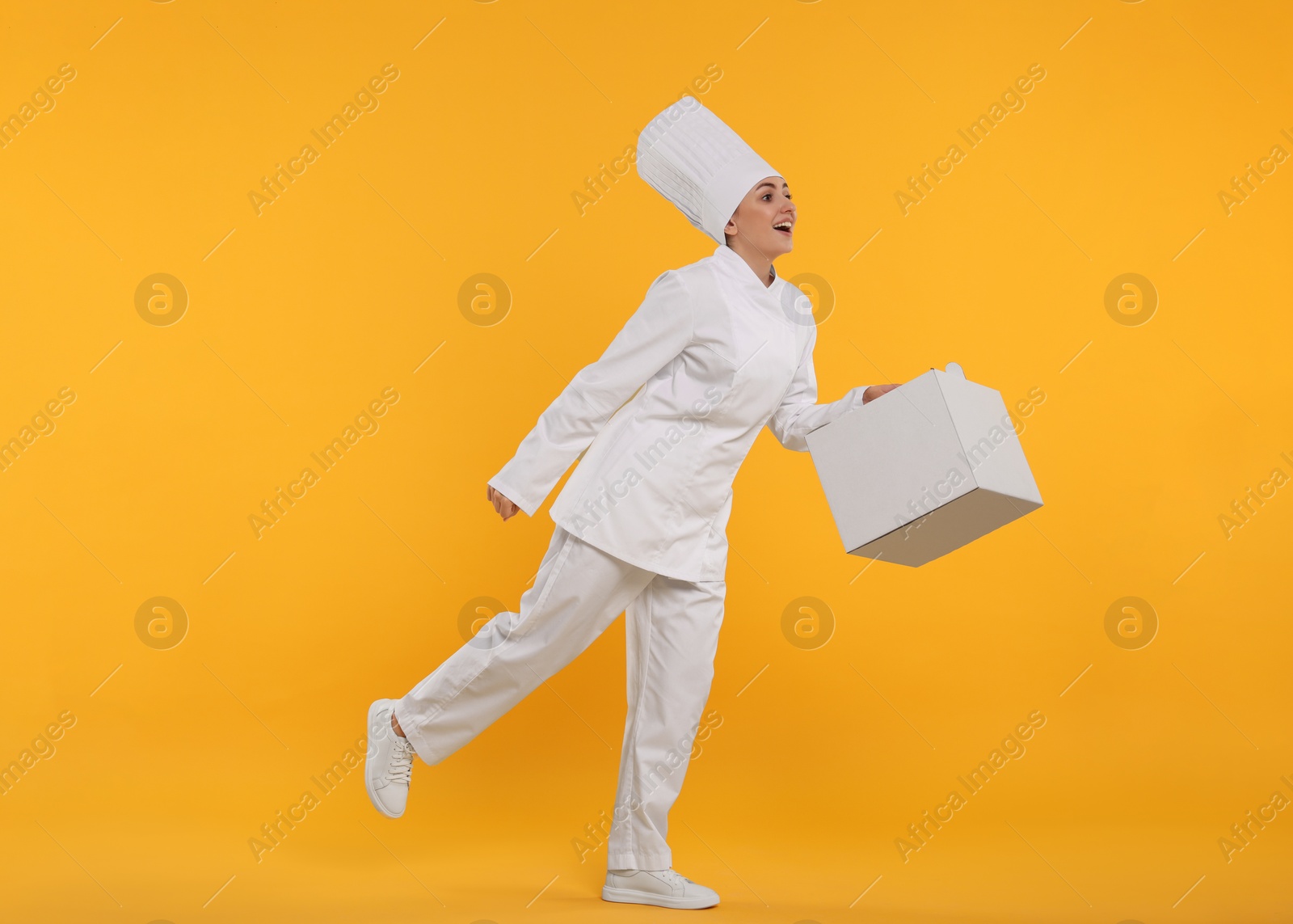 Photo of Happy professional confectioner in uniform holding cake box on yellow background