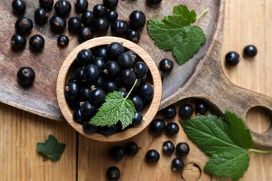 Photo of Ripe blackcurrants and leaves on wooden table, flat lay