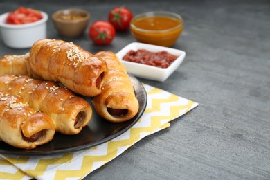 Photo of Delicious sausage rolls and ingredients on grey table, closeup. Space for text