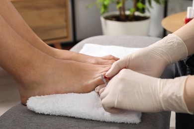 Photo of Pedicurist cutting client`s toenails with scissors in beauty salon, closeup