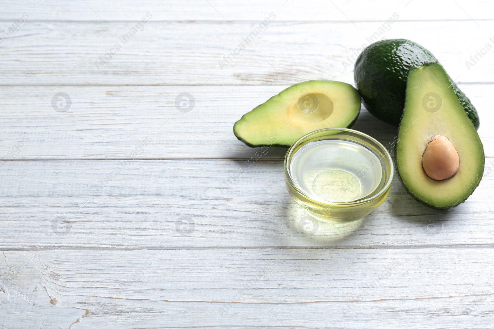 Photo of Bowl of natural oil and avocados on white wooden background. Space for text