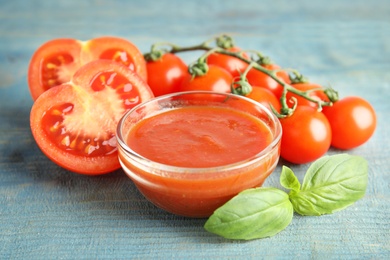 Photo of Bowl of sauce with basil and tomatoes on wooden table, closeup