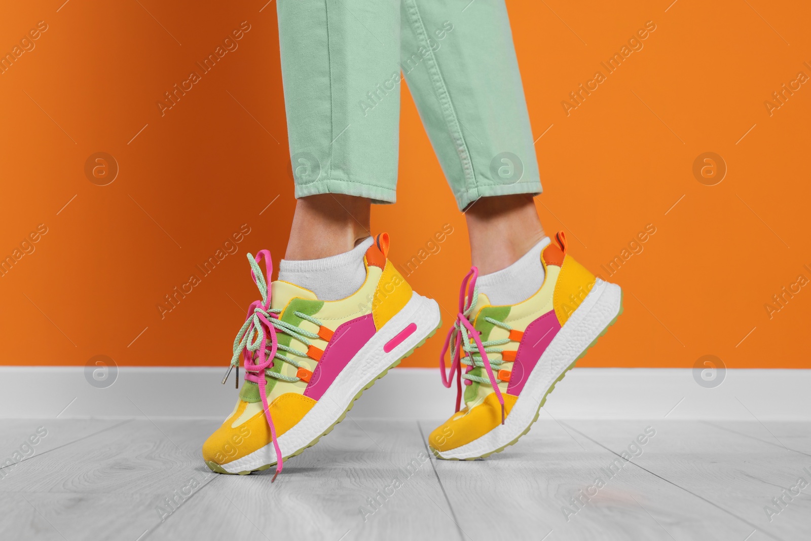 Photo of Woman wearing pair of new stylish sneakers near orange wall, closeup