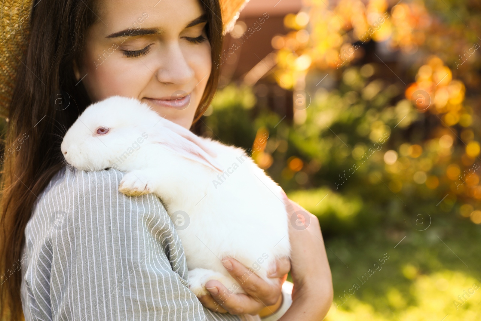 Photo of Happy woman with cute rabbit outdoors on sunny day, closeup. Space for text